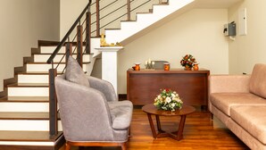 Un escalier avec une rampe en métal, un fauteuil gris, une table basse en bois agrémentée d’un arrangement floral et un canapé beige dans un salon.