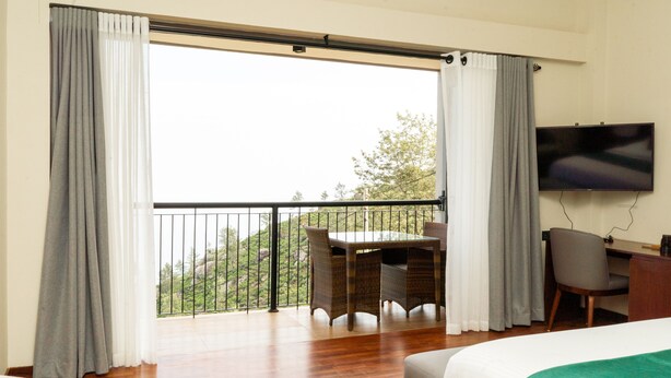 Une chambre d’hôtel avec un balcon, un lit, une télévision et un coin repas aménagé avec des meubles en osier.