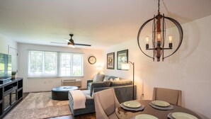A modern living room with a sofa, dining table, and a ceiling fan. - Community Pool Near Lake Como Interlaken for 6 (Lake Geneva)
