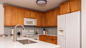 A kitchen with wooden cabinets, a white refrigerator, a microwave, a stove, and a sink. - Community Pool Near Lake Como Interlaken for 6 (Lake Geneva)