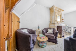 Un salon avec deux fauteuils en cuir, une petite table ronde sur laquelle repose un livre, un miroir décoratif et une cheminée.