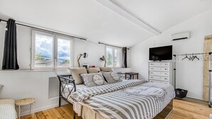 A bedroom with a bed, a TV, a desk, and a window with curtains.