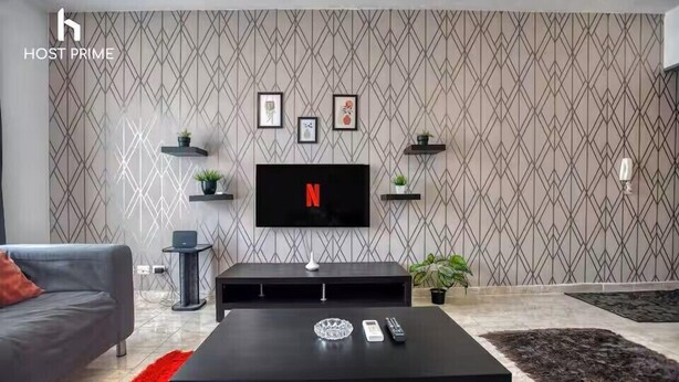 En moderne stue med et fladskærms-tv på væggen, en grå sofa, et sort sofabord og en rød måtte.