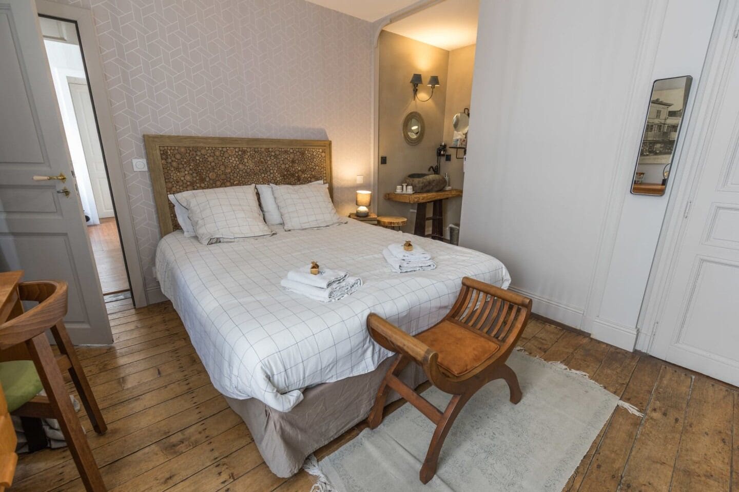 Ein ordentlich eingerichtetes Schlafzimmer mit einem großen Bett, einem Holzstuhl, einem Nachttisch und einem Spiegel an der Wand.
