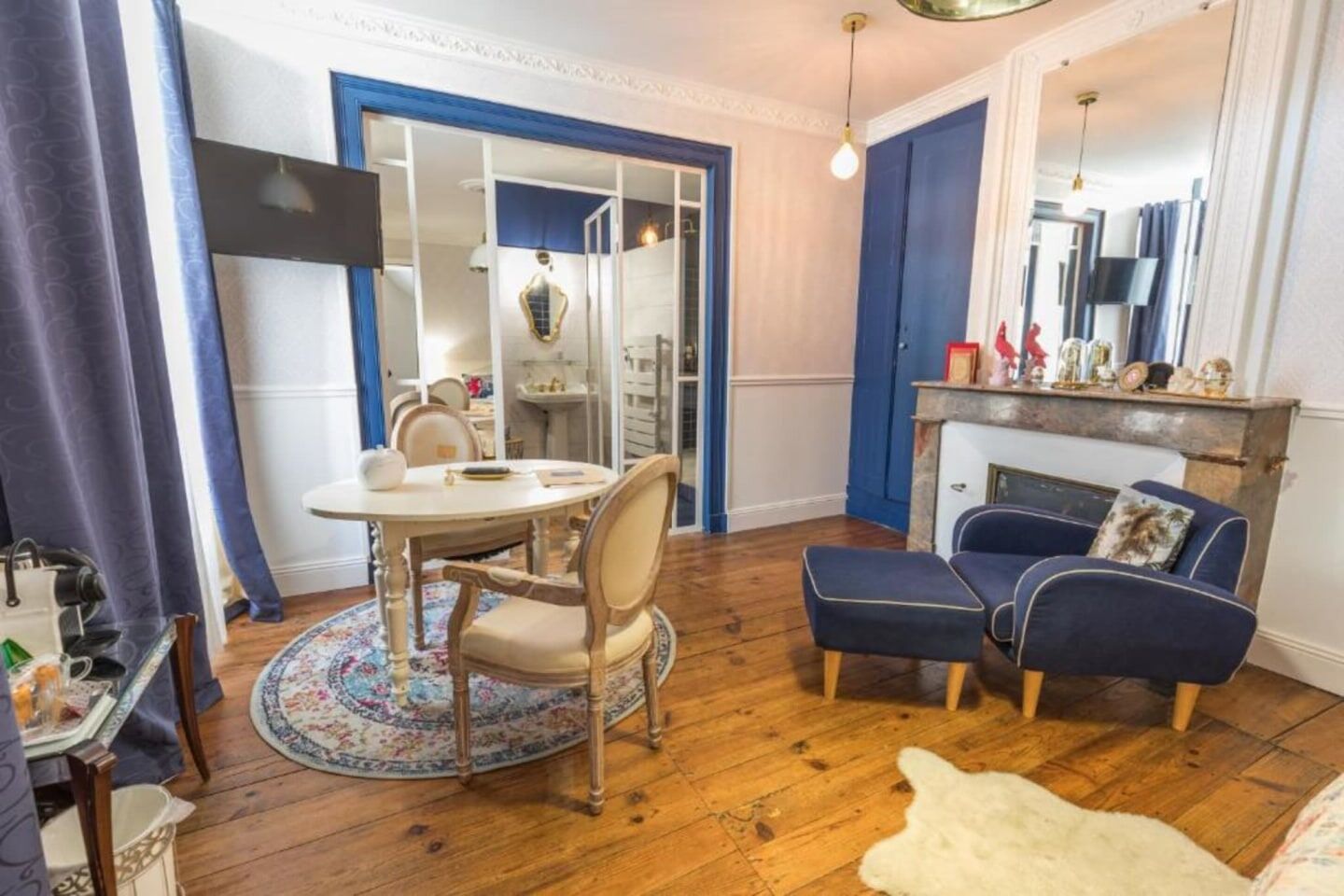 Ein Zimmer mit einem runden Esstisch, zwei Stühlen, einem blauen Sofa, einem weißen Fellteppich und Holzböden.