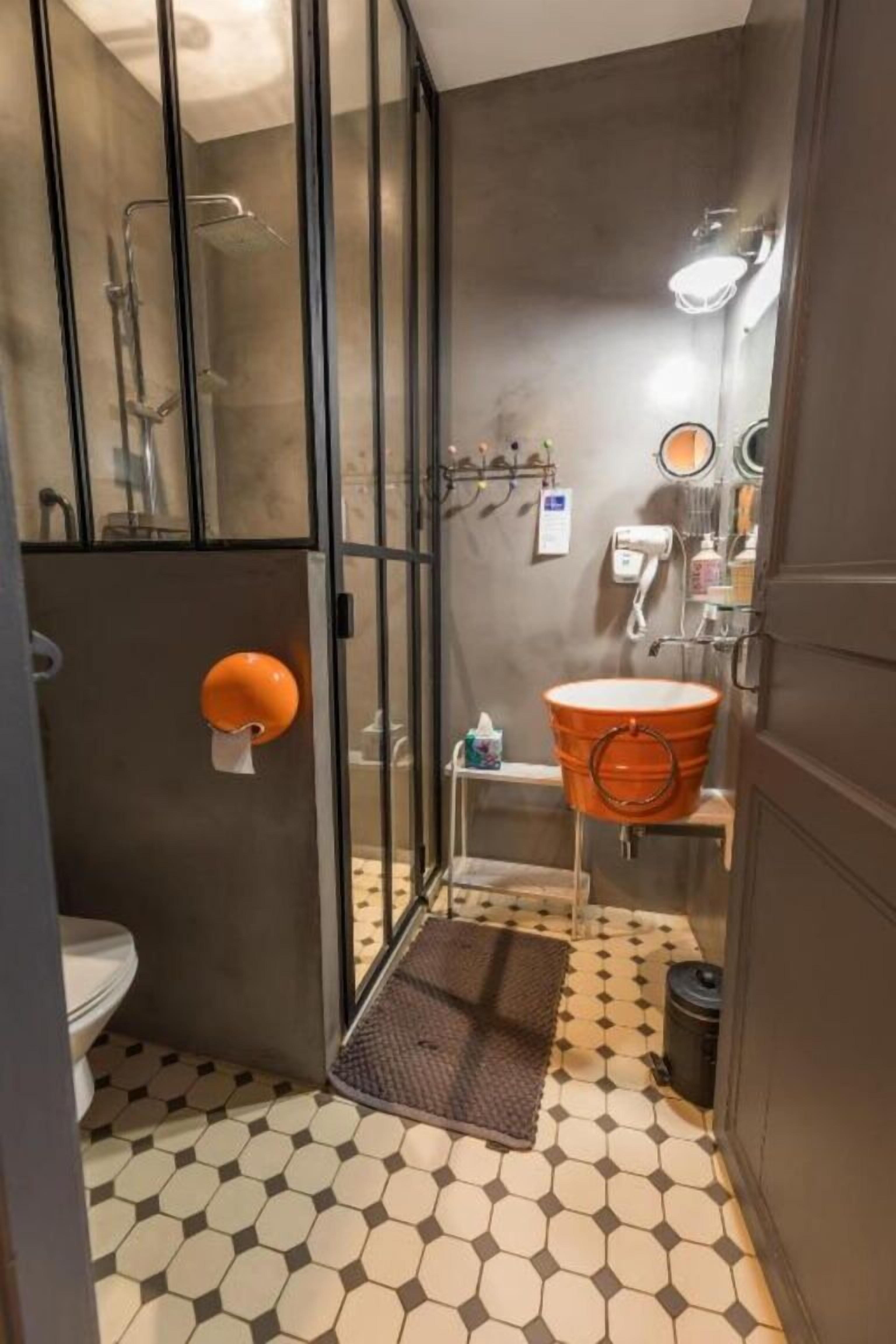 A bathroom with a glass shower enclosure, a toilet, a sink with a large orange basin, and a patterned floor.