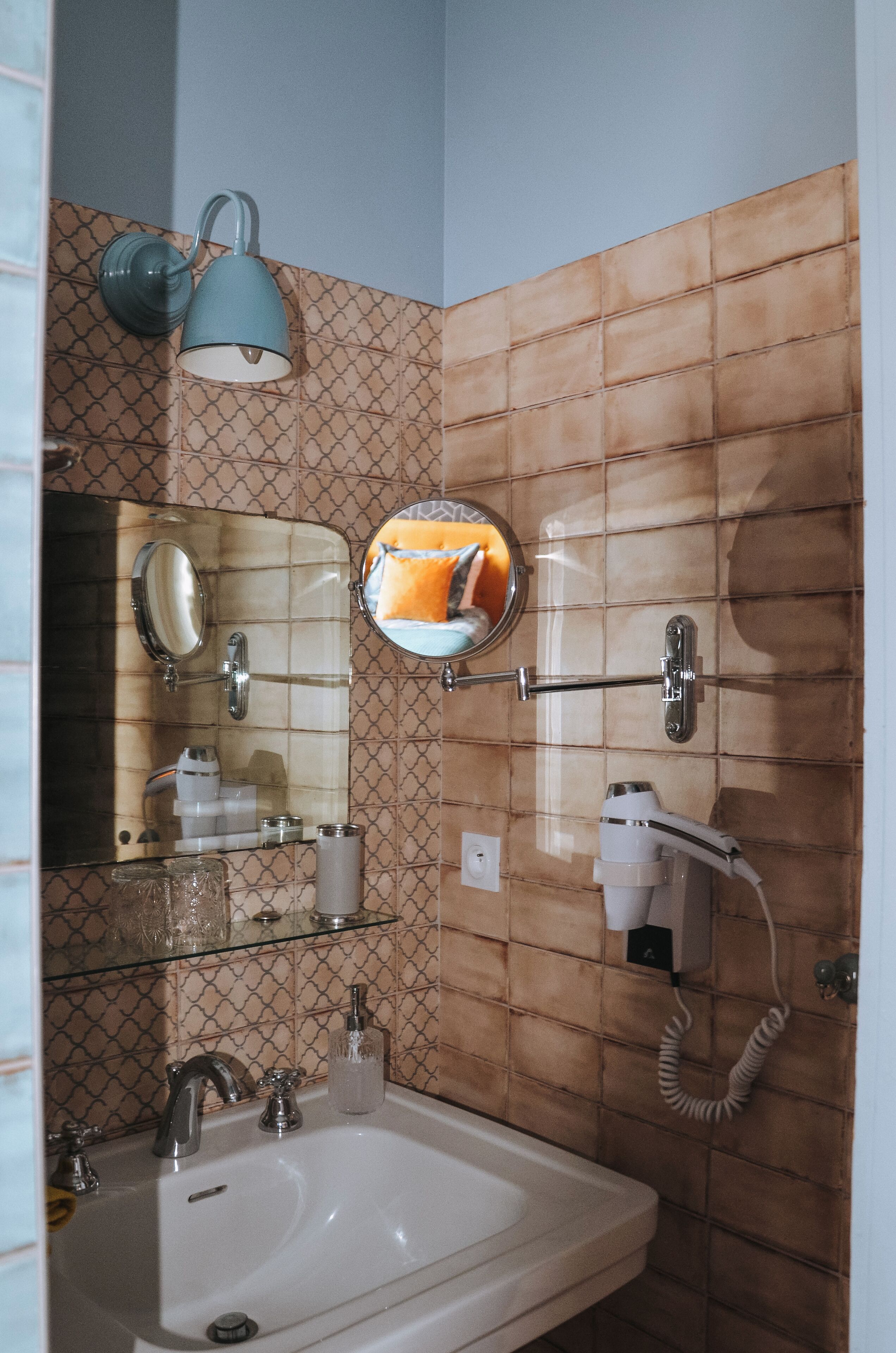 Ein Badezimmer mit Waschbecken, Spiegel, Handtuchhalter, Spender für Handtücher, Fön und einer Wandleuchte.