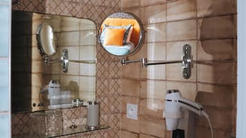 Ein Badezimmer mit Waschbecken, Spiegel, Handtuchhalter, Spender für Handtücher, Fön und einer Wandleuchte.
