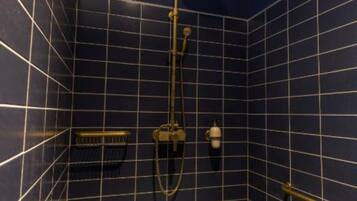 Un baño pequeño revestido de azulejos azul oscuro, con ducha de cabeza dorada e hidromasaje manual.