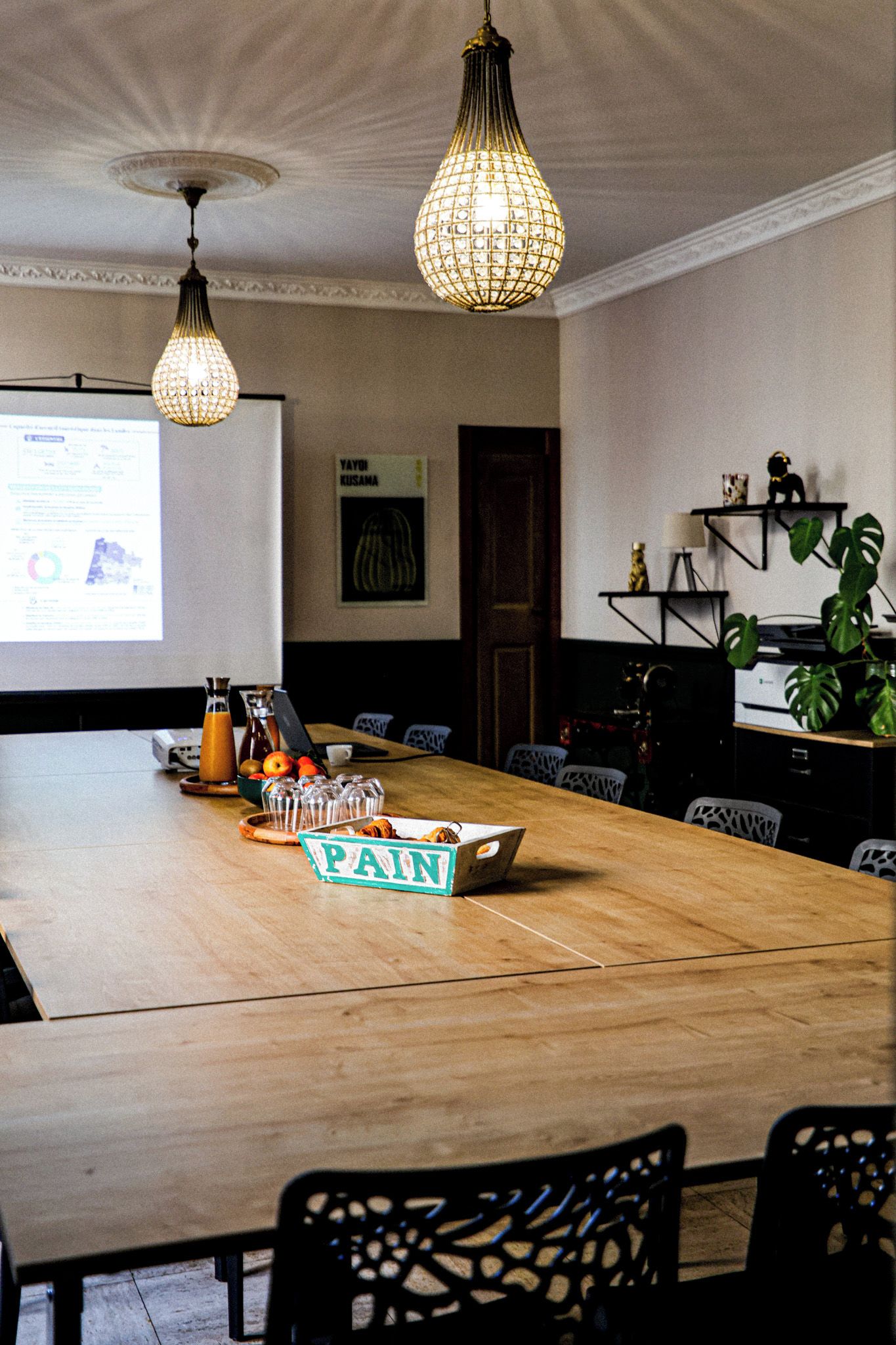 Una sala de conferencias con una larga mesa, sillas, una pantalla de proyector y una lámpara decorativa.