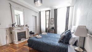 Une chambre d’hôtel avec un grand lit, une cheminée, un bureau avec une lampe et une chaise.