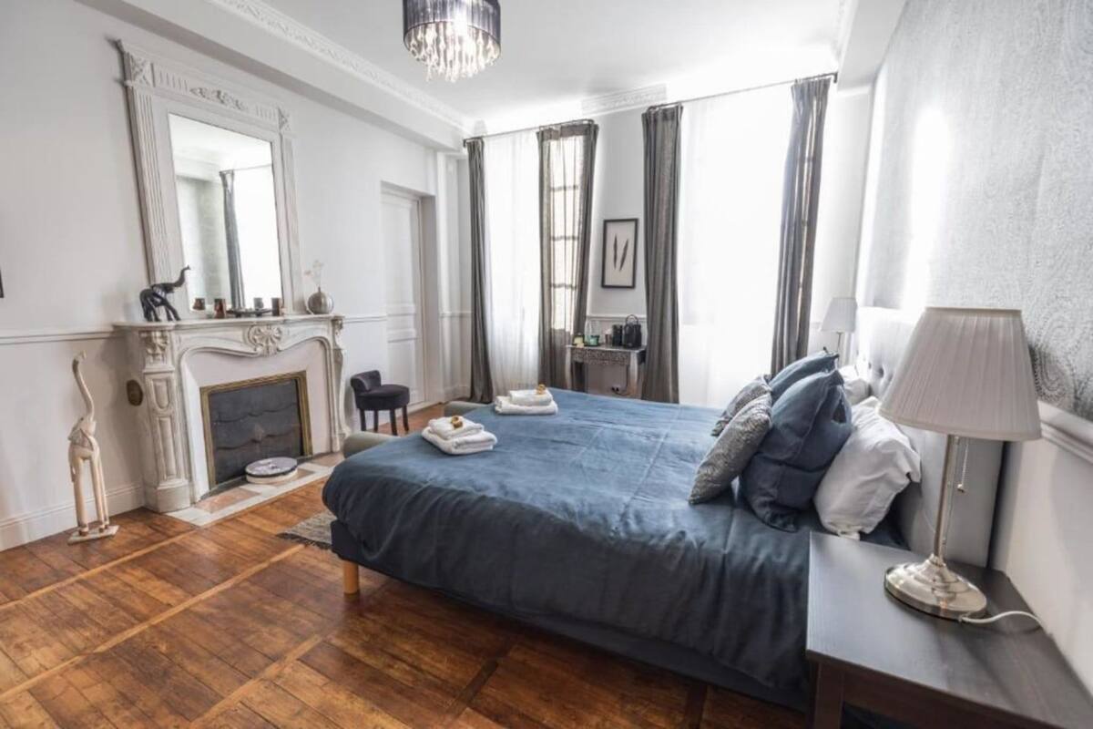 Una habitación de hotel con una cama grande, una chimenea, un escritorio con una lámpara y una silla.