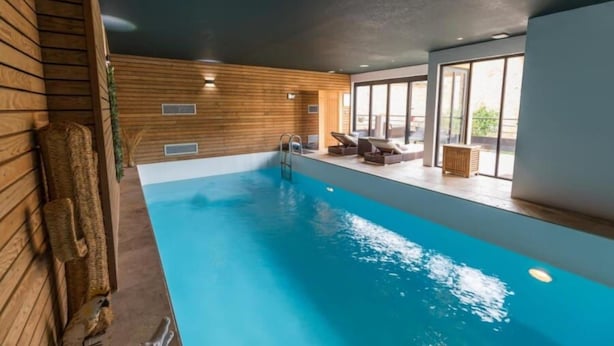 Une piscine intérieure aux murs en bois, avec un escalier et un espace détente offrant une vue sur l’extérieur.