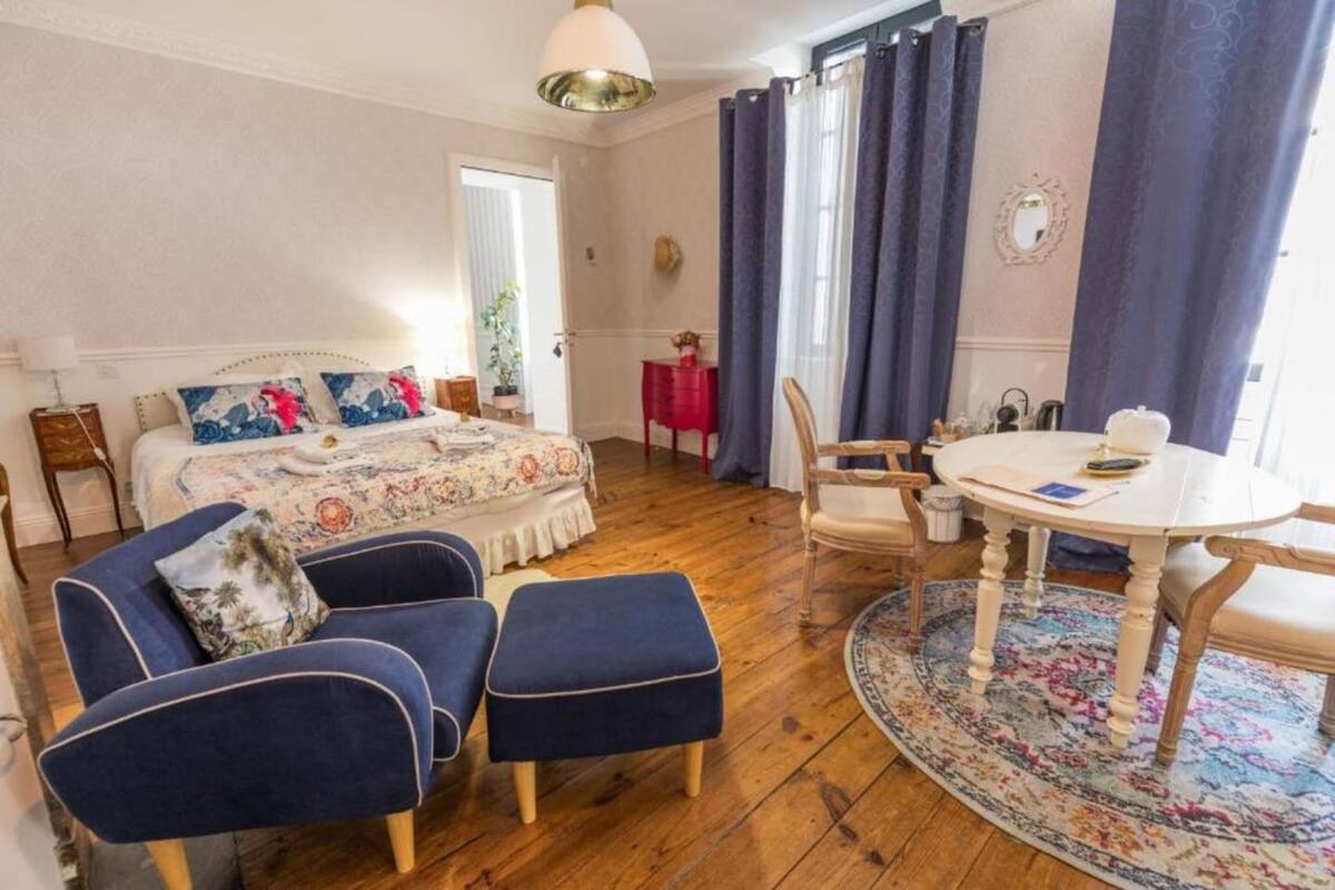 Un dormitorio con cama, zona de estar con mesa y sillas, y ventana con cortinas.