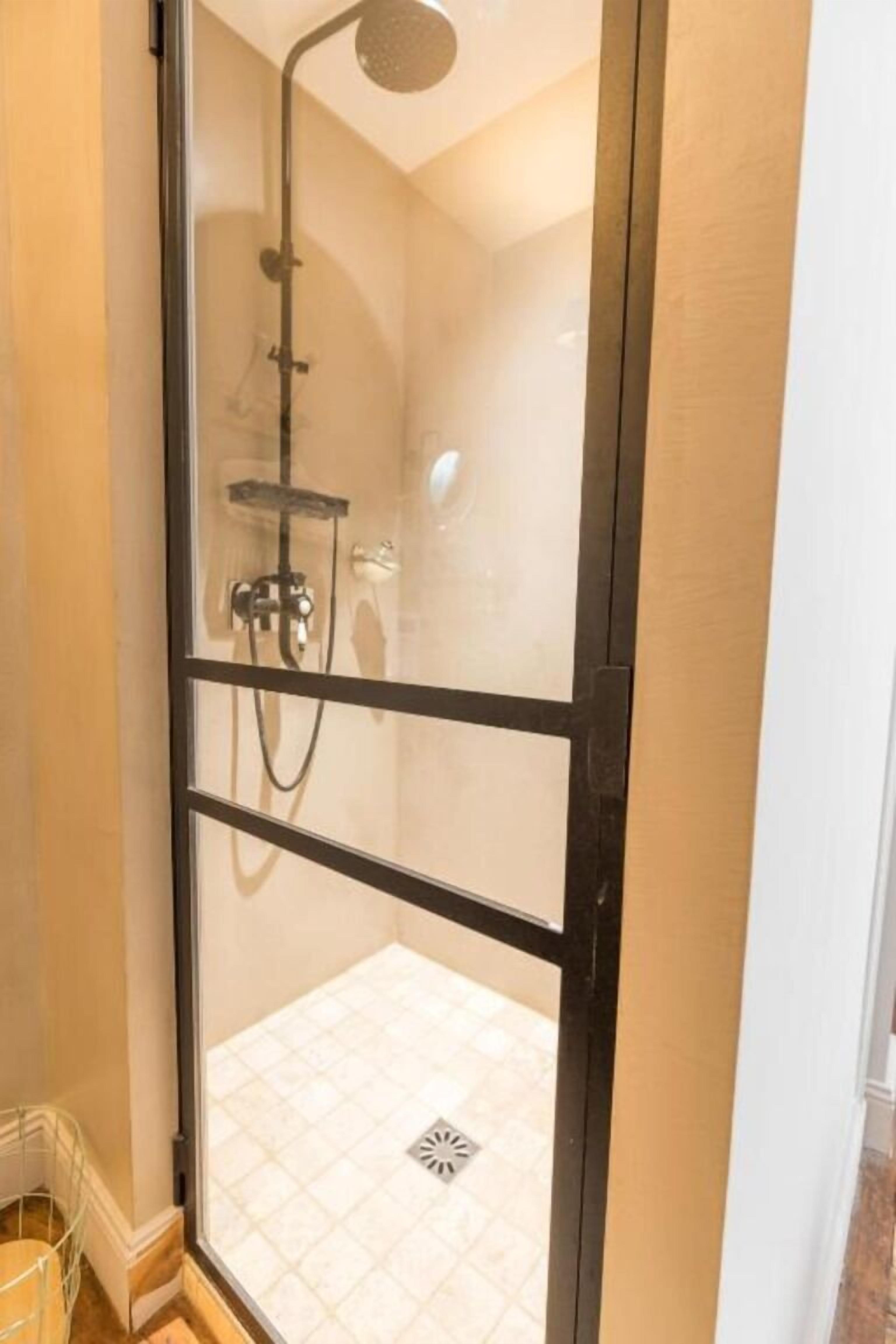 Une douche fermée par des parois en verre, dotée d’un pommeau de douche à main et d’un robinet mural.