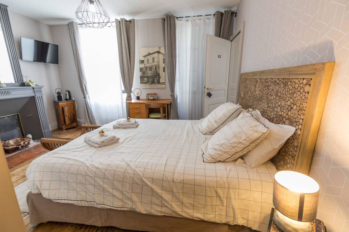 Una cama bien tendida con un edredón a cuadros, una lámpara de noche y un televisor montado en la pared.