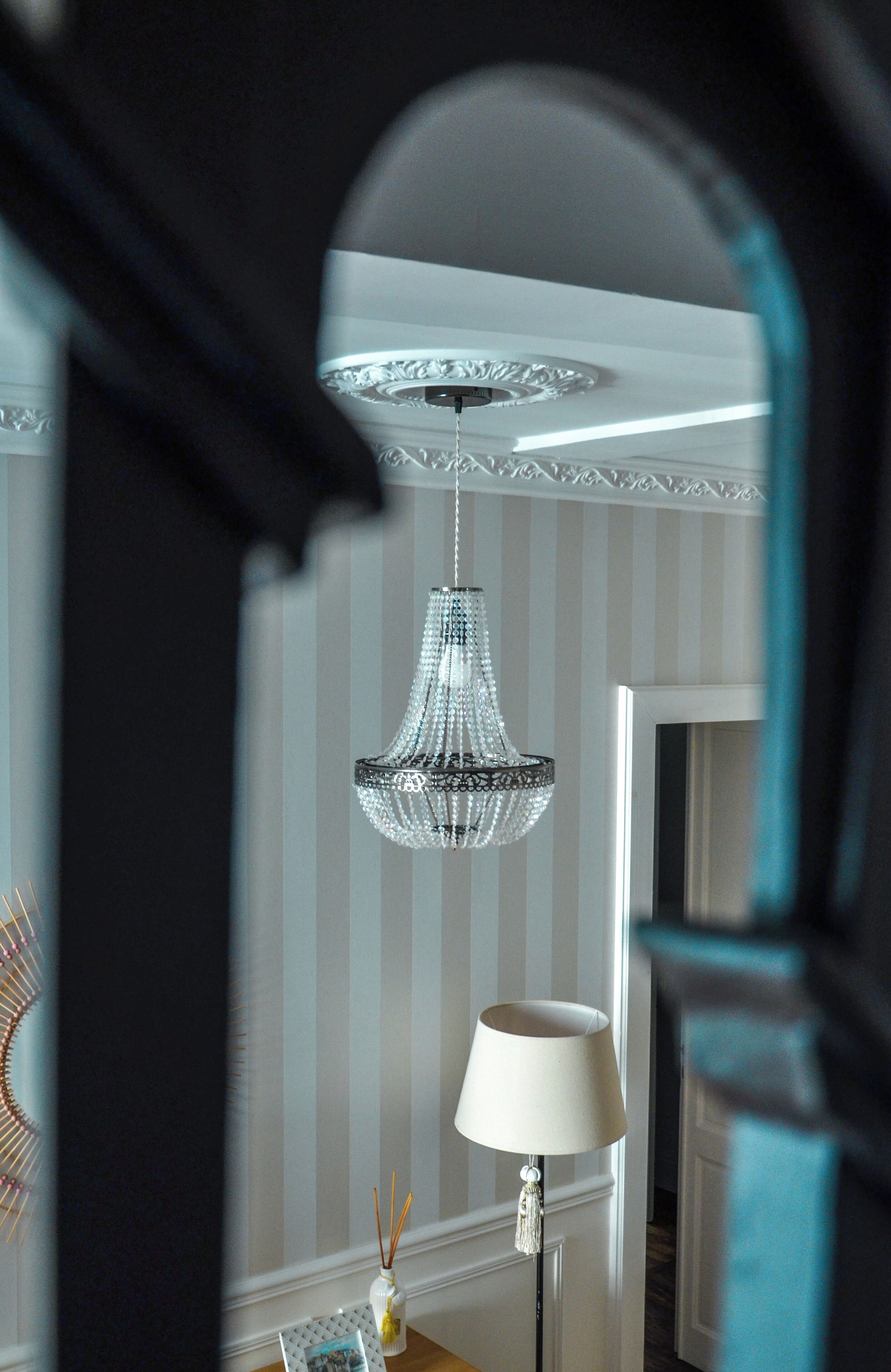 A chandelier in a room with striped wallpaper and a lamp.