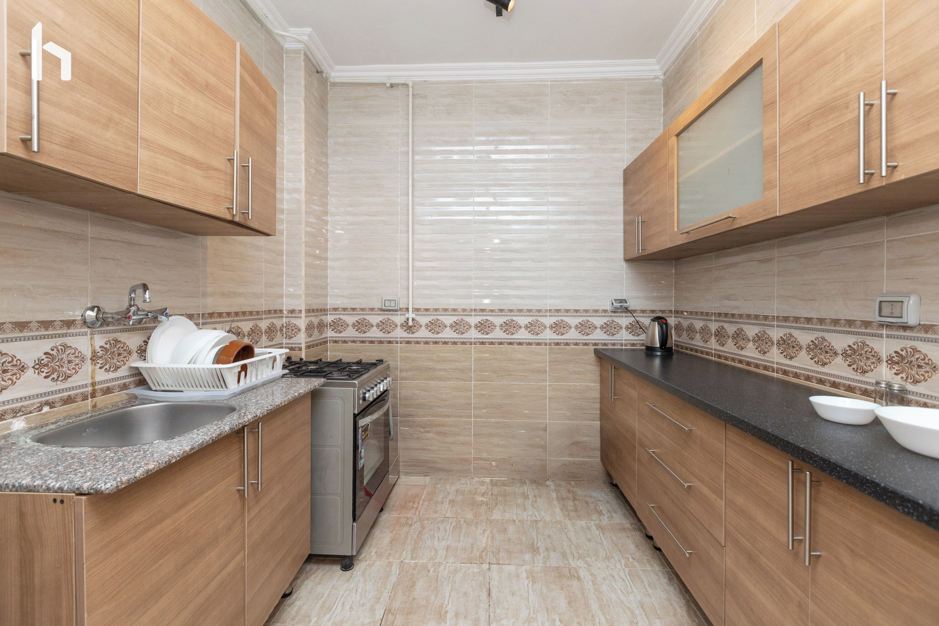 Una cocina con gabinetes de madera, encimera de granito, pileta de acero inoxidable y horno empotrado.
