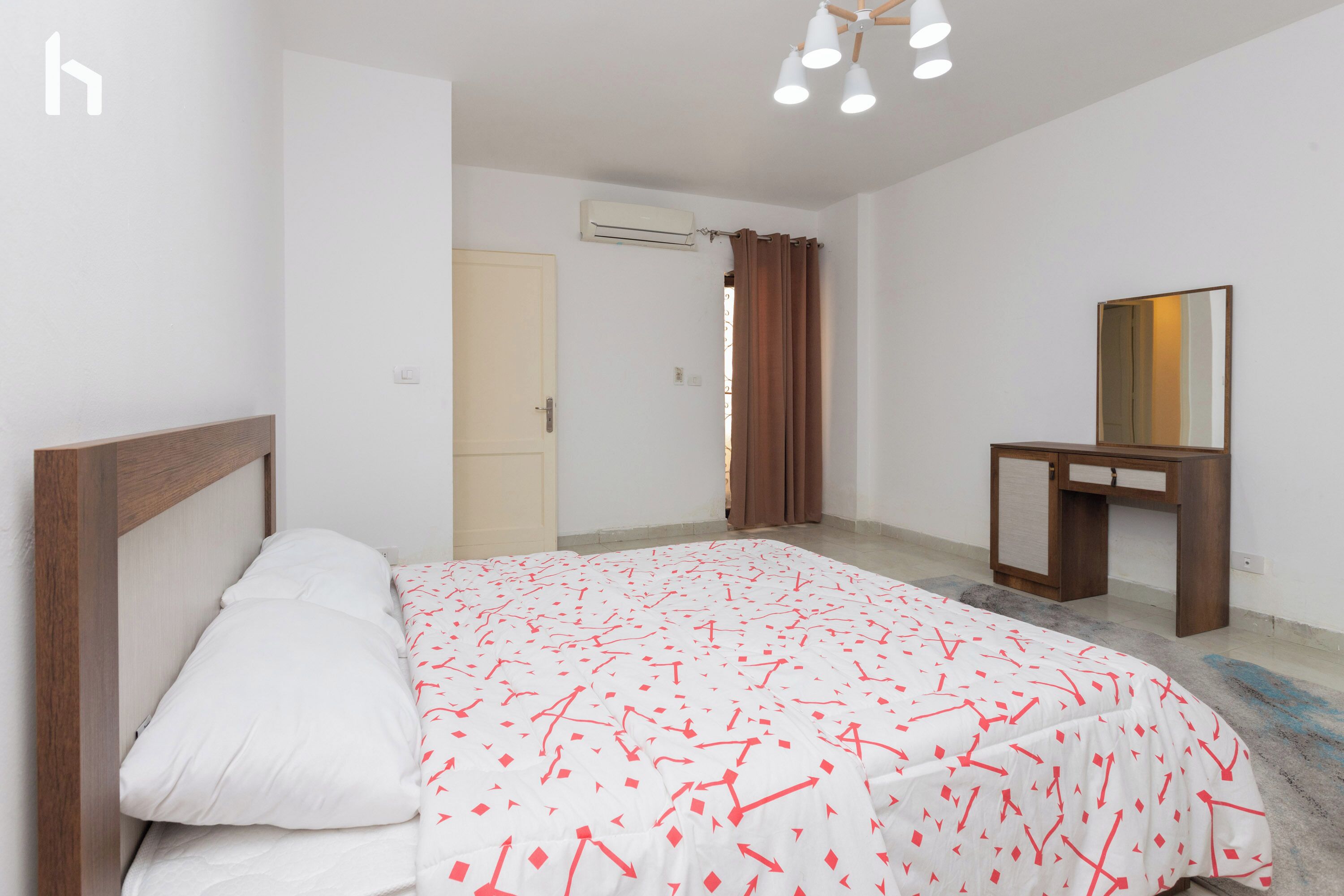 A bedroom with a bed, a desk, a mirror, and an air conditioning unit.