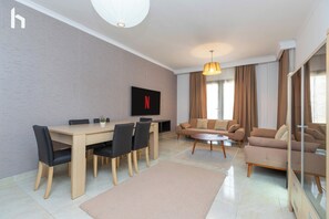 A modern living room with a dining area, a sofa set, and a flat-screen TV mounted on the wall. - Family stay Apartment in Rehab city (New Cairo)