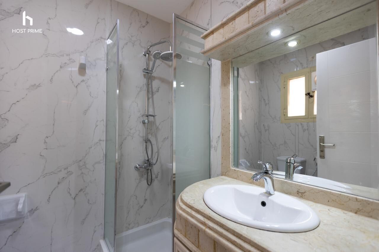 A bathroom with a glass-enclosed shower, a white sink, and a large mirror.