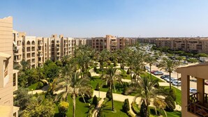 A hotel with multiple floors, a parking area, and a well-maintained garden with palm trees. - Cozy (New Cairo)