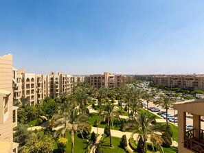A hotel with multiple floors, a parking area, and a well-maintained garden with palm trees. - Cozy (New Cairo)