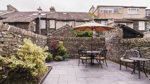 A patio area with stone walls, a table with chairs, and potted plants. - Herdwick Cottage, Stylish 3 bed, Central Ambleside (Ambleside)