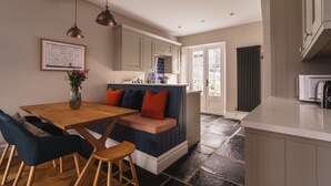 A modern kitchen with a wooden dining table, a built-in bench with cushions, and a pendant light. - Herdwick Cottage, Stylish 3 bed, Central Ambleside (Ambleside)