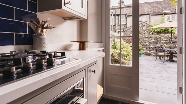 A kitchen with a gas stove, white cabinets, and a view of the outdoor patio through a glass door. - Herdwick Cottage, Stylish 3 bed, Central Ambleside (Ambleside)