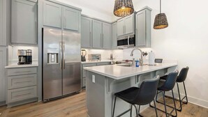 A modern kitchen with grey cabinets, stainless steel appliances, a central island with bar stools, and pendant lighting.