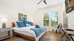 A bedroom with a bed, bedside tables, a chair, a desk, and a window with blinds.