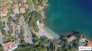 Vista aérea de uma área costeira com praia, carros estacionados e edifícios com telhados vermelhos.
