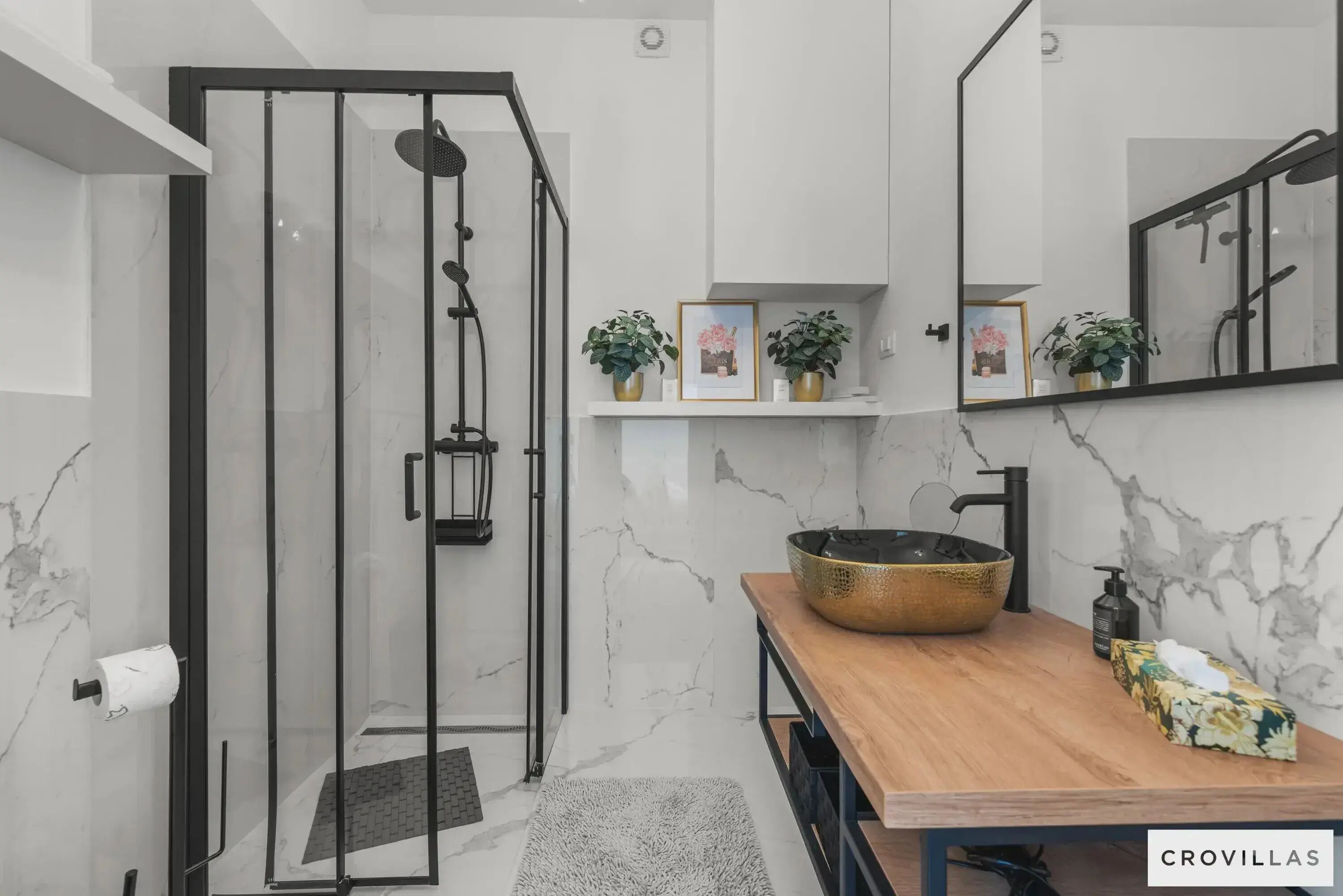 Une salle de bain moderne dotée d’une douche à parois de verre, de murs en marbre, d’un meuble-lavabo en bois avec un grand lavabo en cuvette et d’un miroir au-dessus du lavabo.