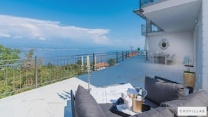 Terraço com vista para o mar, mobiliado com sofás cinzentos e uma mesa com uma garrafa e copos.