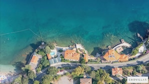Vista aérea de uma área residencial costeira com casas, águas azul-claras e uma estrada.