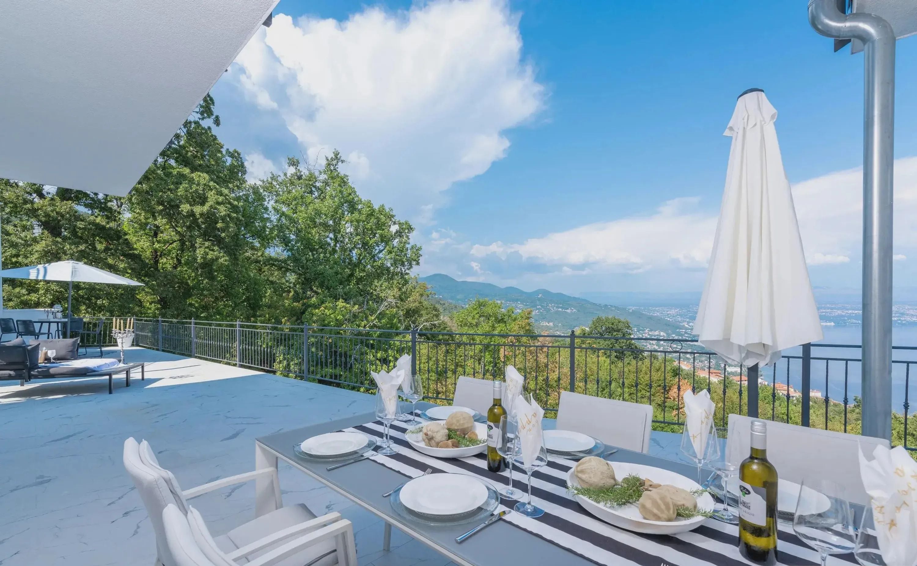 A dining table set with plates, glasses, and a bottle, overlooking a scenic landscape.