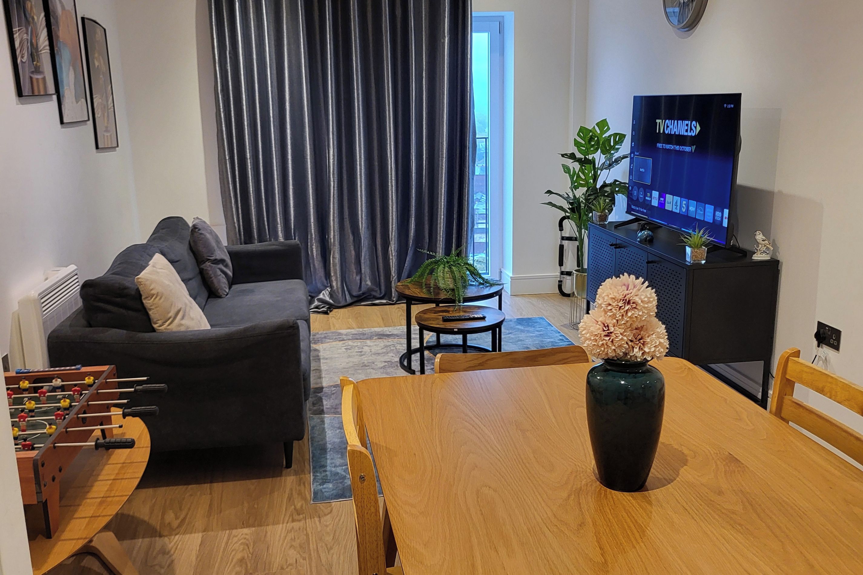 A living room with a sofa, a dining table, a TV, and a foosball table.