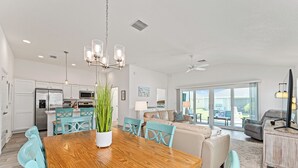 Un vaste espace de vie comprenant une table à manger en bois, des chaises de couleur turquoise et un canapé beige.