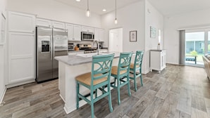 Une cuisine moderne avec des meubles blancs, des appareils en acier inoxydable et des chaises de couleur turquoise.