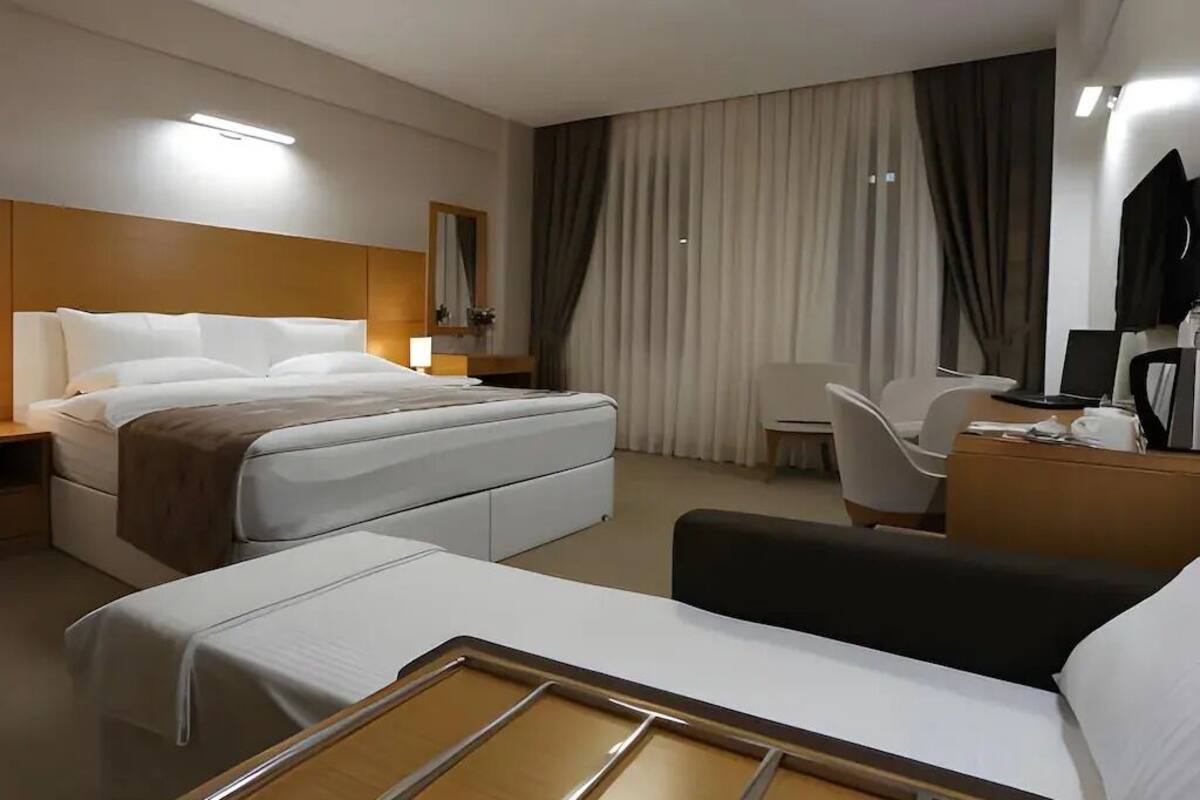 Habitació d'hotel moderna amb llit, taulella de nit, cadira, escriptori i un mirall gran.
