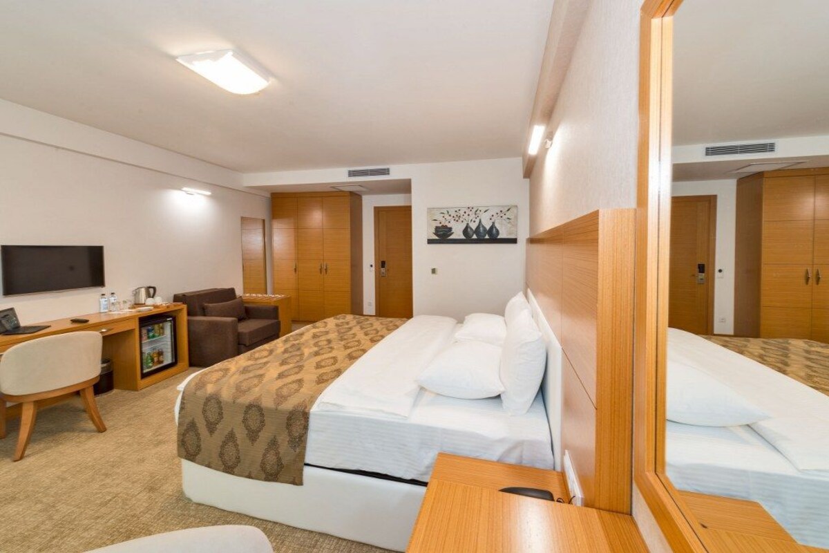 A hotel room with a bed, a desk, a chair, a TV, and a small refrigerator.