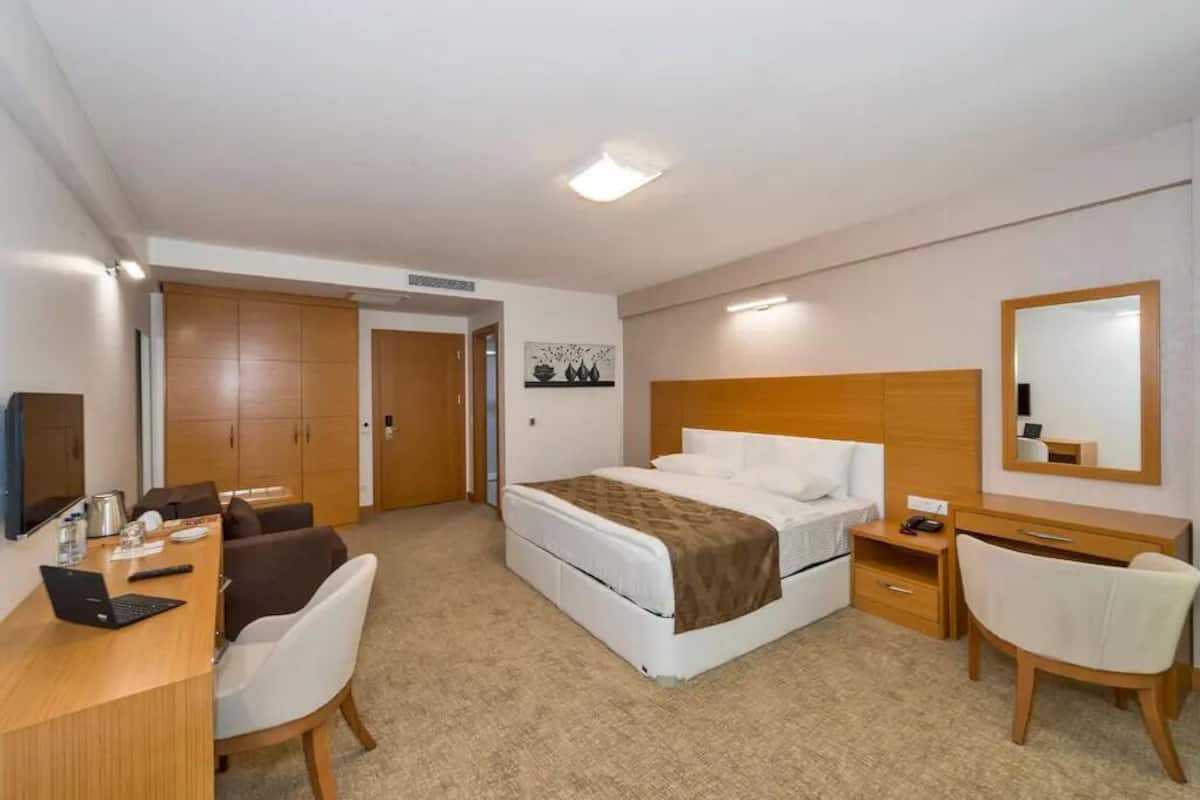 Una habitació d'hotel amb un llit, una taula de treball amb un ordinador portàtil, una cadira, una tauleta de nit i un armari.