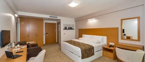 A hotel room with a bed, a desk with a laptop, a chair, a bedside table, and a wardrobe.