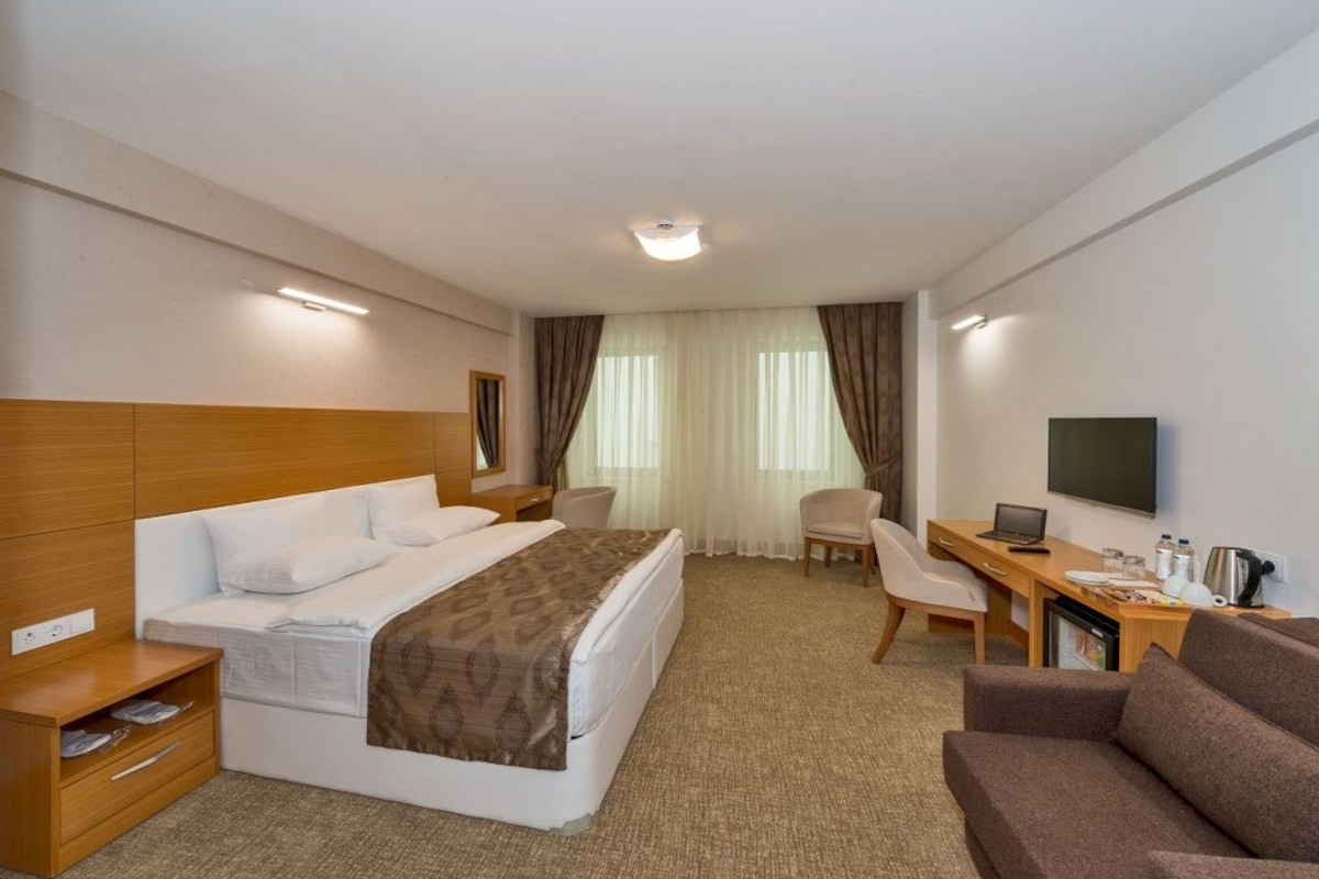 A hotel room with a bed, a desk with a laptop, a TV, and a seating area.