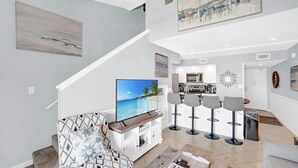 Un salon moderne avec un téléviseur à écran plat, un canapé et une table basse. Un escalier mène à un niveau supérieur.