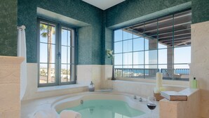 A bathroom with a large bathtub, a window with a view, and a towel on the floor.