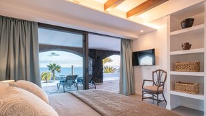 A bedroom with a large bed, a TV, and a view of the sea.