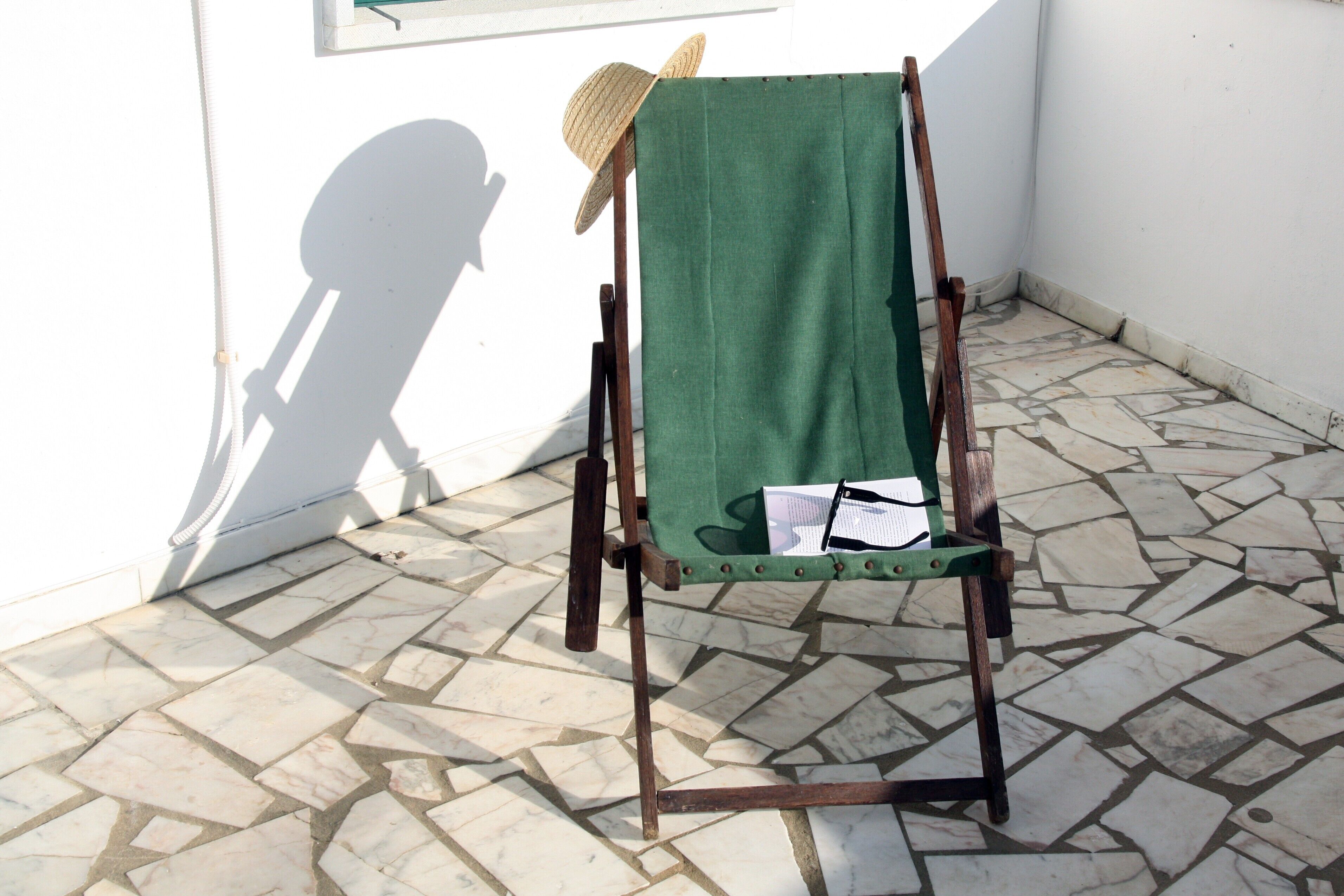 A wooden easel with a green cloth backdrop, a straw hat, and papers on it, positioned on a tiled floor.
