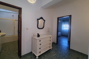 A hallway with a white dresser, a mirror, and a door leading to another room.